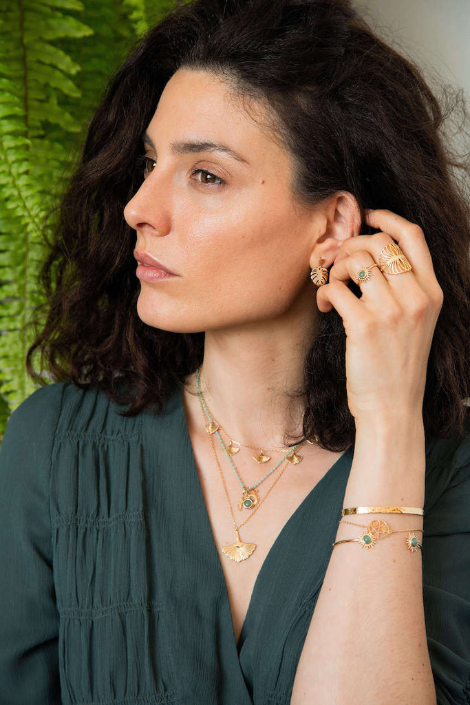 Une femme porte plusieurs colliers et bracelets en plaqué or, mettant en valeur des pendentifs en forme de feuille de ginkgo et de ravissantes pierres naturelles.