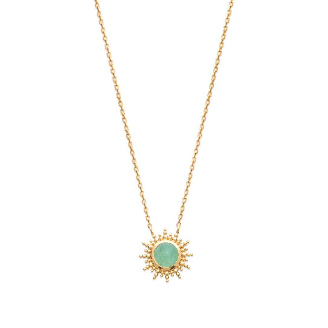 Détail d'un pendentif soleil en plaqué or orné d'un quartz vert sur un collier pour femme.